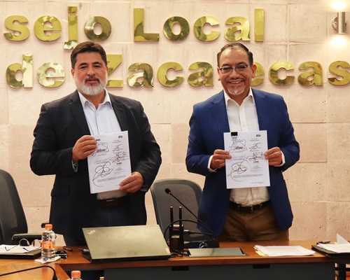 Dos hombres de pie sosteniendo un documento, mirando al frente
