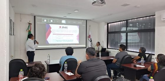 Personas en un salón viendo una pantalla con imagen del INE en Quintana Roo