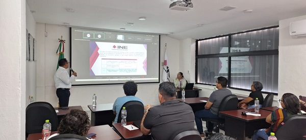 Personas en un salón viendo una pantalla con imagen del INE en Quintana Roo