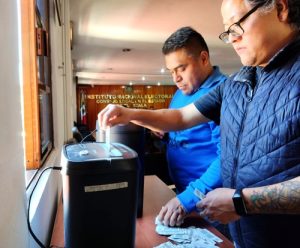 Dos hombres colocando credenciales para votar en una trituradora