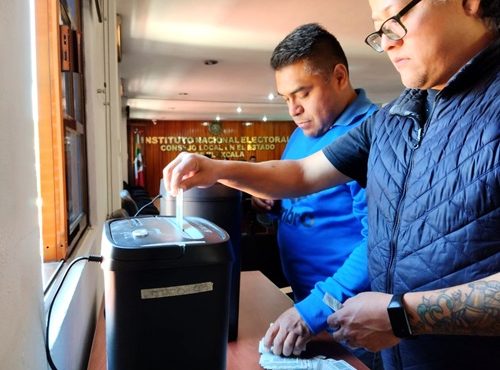 Dos hombres colocando credenciales para votar en una trituradora