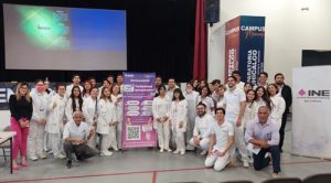 Personas de píe e hincados alrededor de un cartel del INE