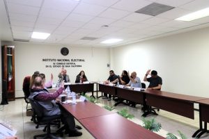 personas sentadas en una mesa votando a mano alzada