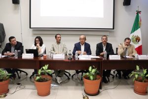seis personas sentadas en una mesa con una bandera de México a un costado