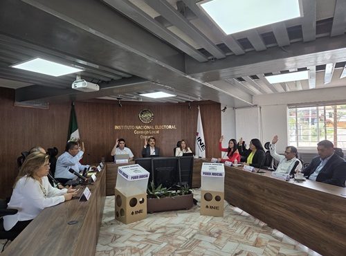 varias personas sentadas votando a mano alzada en el INE de Oaxaca