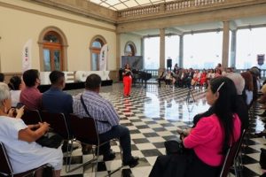 Personas en un Salón con piso a cuadros blanco y negros escuchando un foro