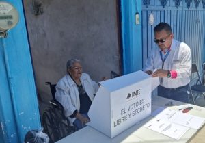 mujer adulta mayor siendo asistida por un hombre para emitir su voto anticipado