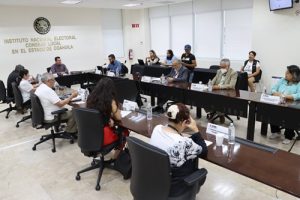 varias personas sentadas alrededor de una mesa ovalada en las instalaciones del INE en Coahuila