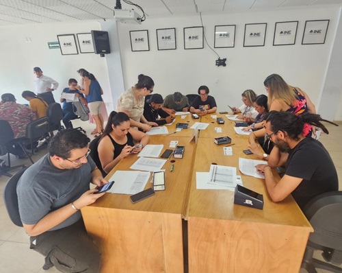 varias personas sentadas alrededor de una mesa, viendo celulares y documentos