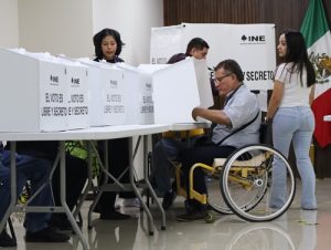 Hombre en silla de ruedas simulando votación en casilla seccional