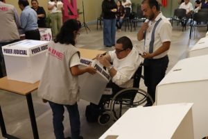 Hombre en silla de ruedas introduciendo boletas en urna con leyenda Poder judicial