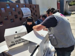Una mujer y un hombre con cubrebocas armando mamparas de votación del INE en Baja California