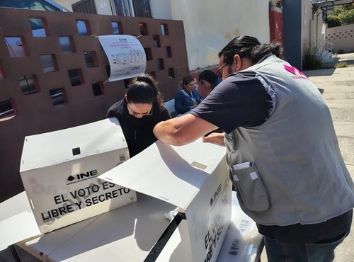 Una mujer y un hombre con cubrebocas armando mamparas de votación del INE en Baja California