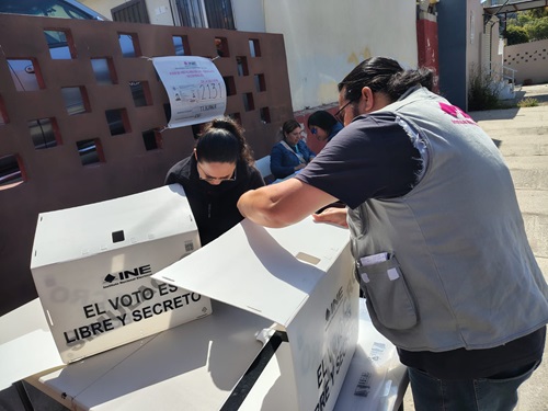 Una mujer y un hombre con cubrebocas armando mamparas de votación del INE en Baja California
