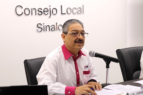 una persona con camisa blanca sentada y hablando con un micrófono
