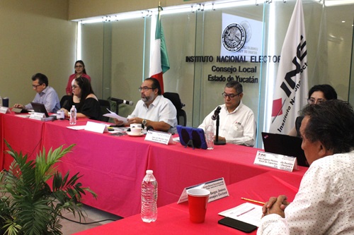 cinco personas sentadas en una mesa con mantel rojo