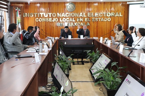 Integrantes del consejo local sentados en salón de sesiones y votando a mano alzada