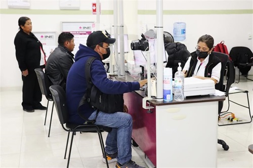 dos personas sentadas en las ventanillas de atención del módulo del INE