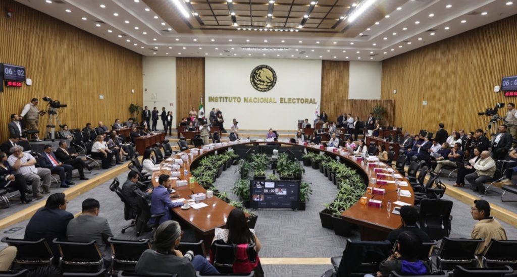 Salón de sesiones con el escudo de México al fondo con letras de color dorado que dice “Instituto Federal Electoral”, mesa en forma de herradura con Consejeros Electorales y representantes de partidos políticos sentados y alrededor de la mesa directores ejecutivos, titulares de unidades técnicas y asesores.