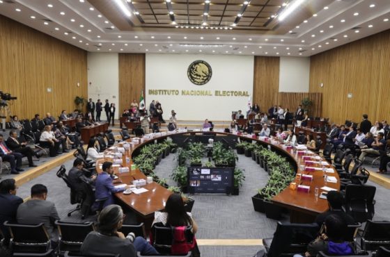 Salón de sesiones con el escudo de México al fondo con letras de color dorado que dice “Instituto Federal Electoral”, mesa en forma de herradura con Consejeros Electorales y representantes de partidos políticos sentados y alrededor de la mesa directores ejecutivos, titulares de unidades técnicas y asesores.