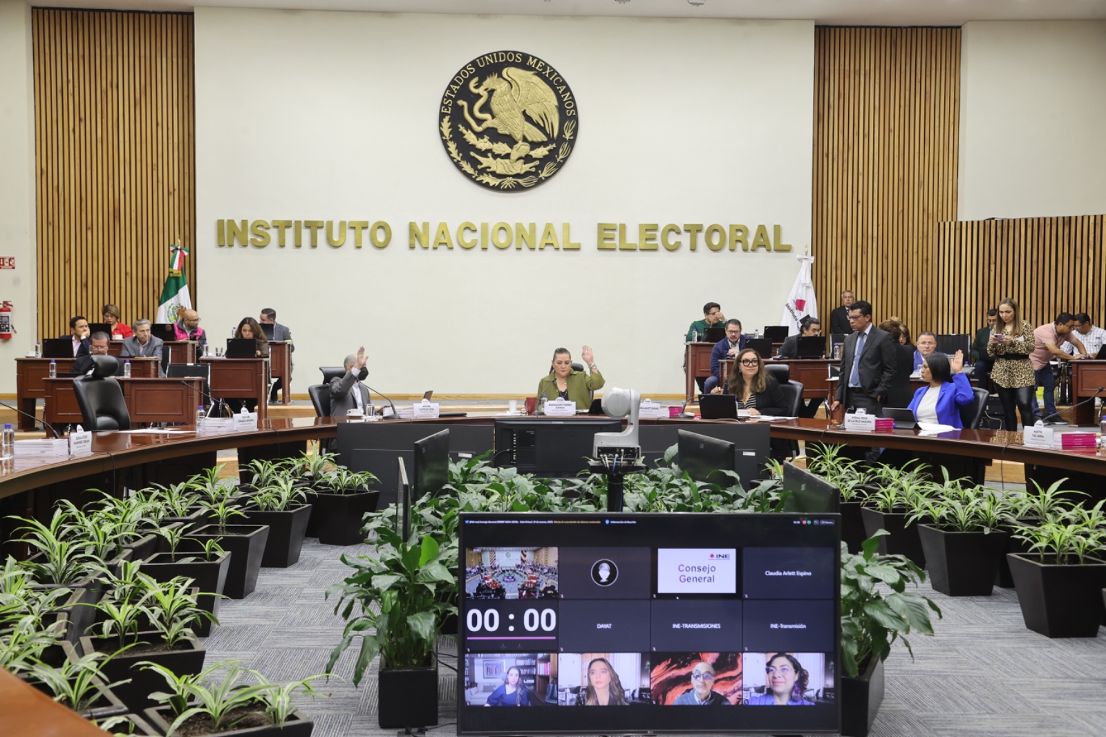 Salón de sesiones y pantalla con recuadros de la participación de las personas Consejeras Electorales.