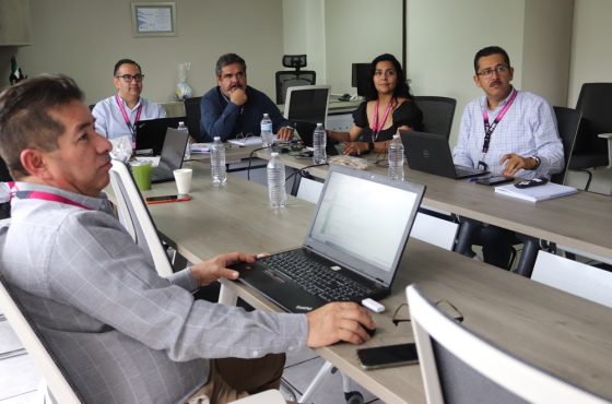 cinco personas sentadas en una mesa mirando una presentación en una pantalla