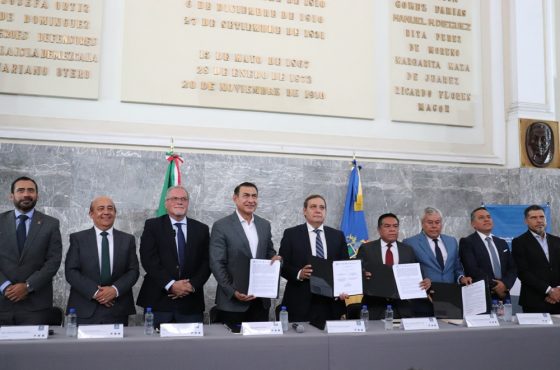 Nueve personas de pie y tres de ellas mostrando el convenio firmado