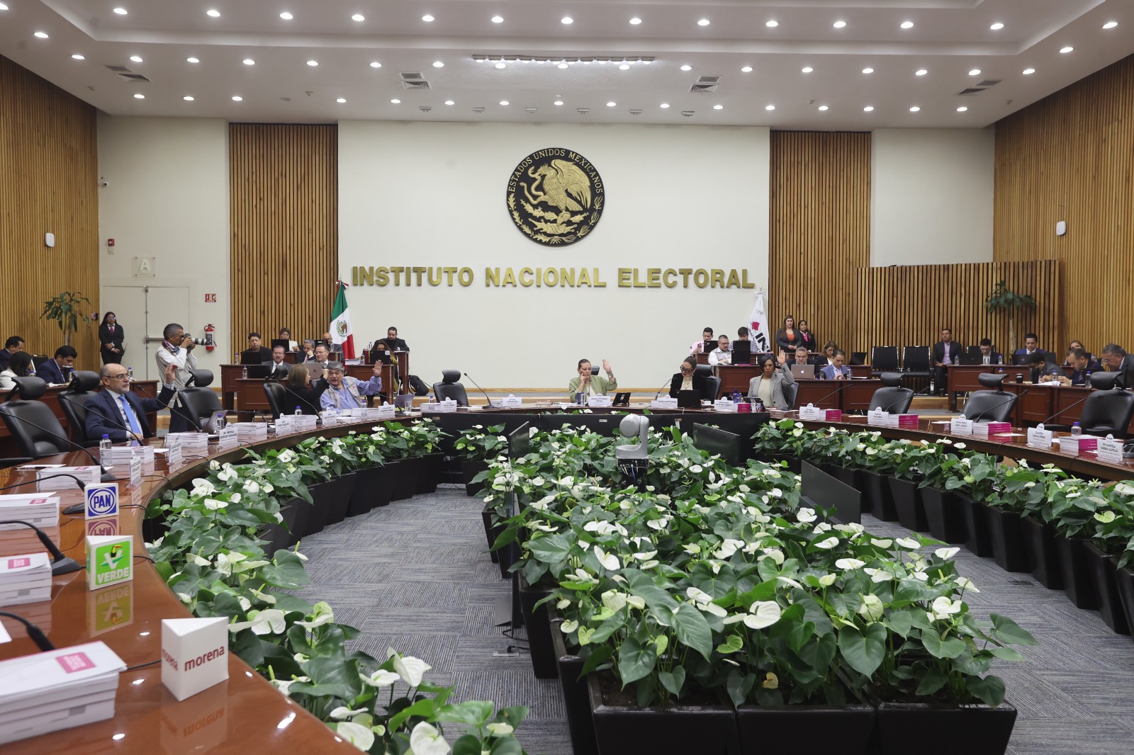 Salón de sesiones del Consejo General del INE del día 2 de julio de 2025. Las y los consejeros levantan la mano para aprobar uno de los acuerdos analizados