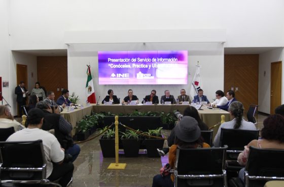 Toma abierta en el lobby del instituto con las personas participantes sentados en el estrado al frente de la audiencia y letrero del evento.