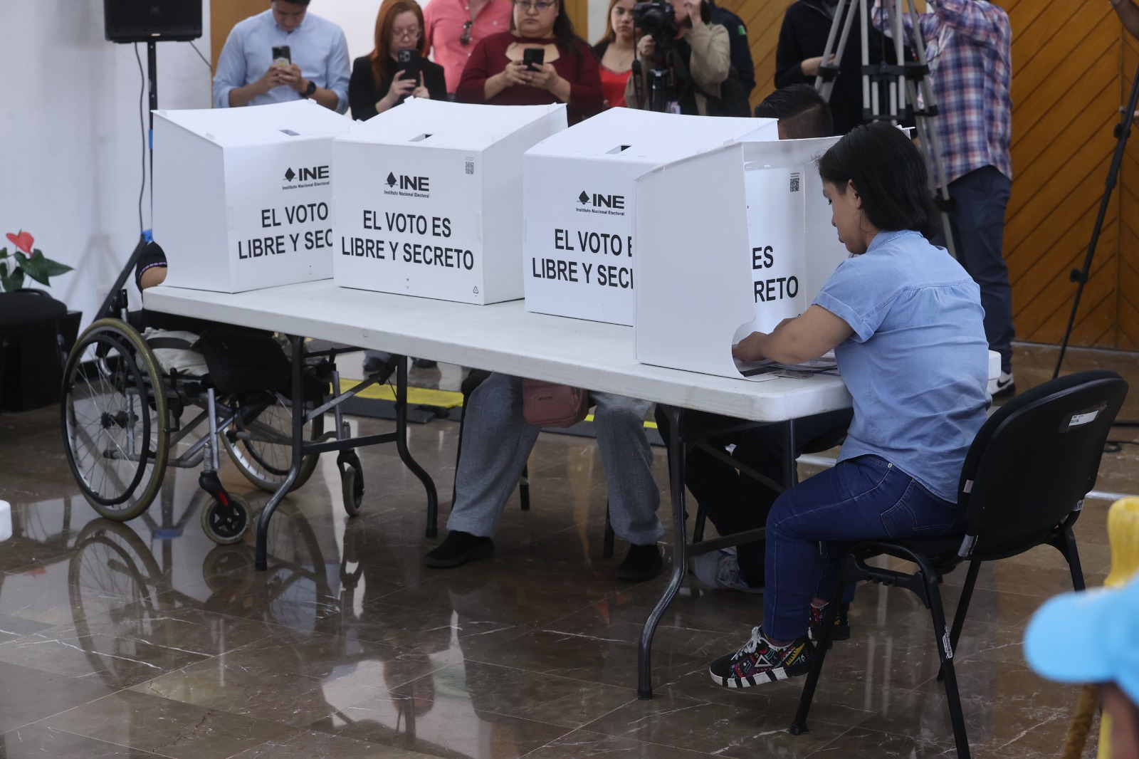 Persona pequeña votando en mampara especial y otra persona votando en mampara especial en silla de ruedas.