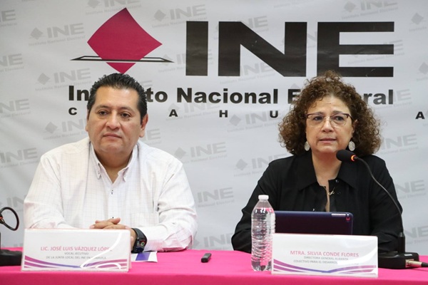 una mujer y un hombre sentados frente a una mesa con mantel rosa