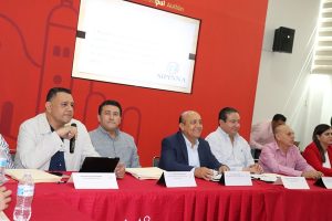 varios hombres sentados frente a una mesa con mantel rojo