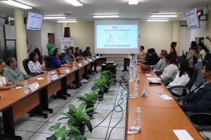 personas sentadas alrededor de una mesa rectangular con micrófonos