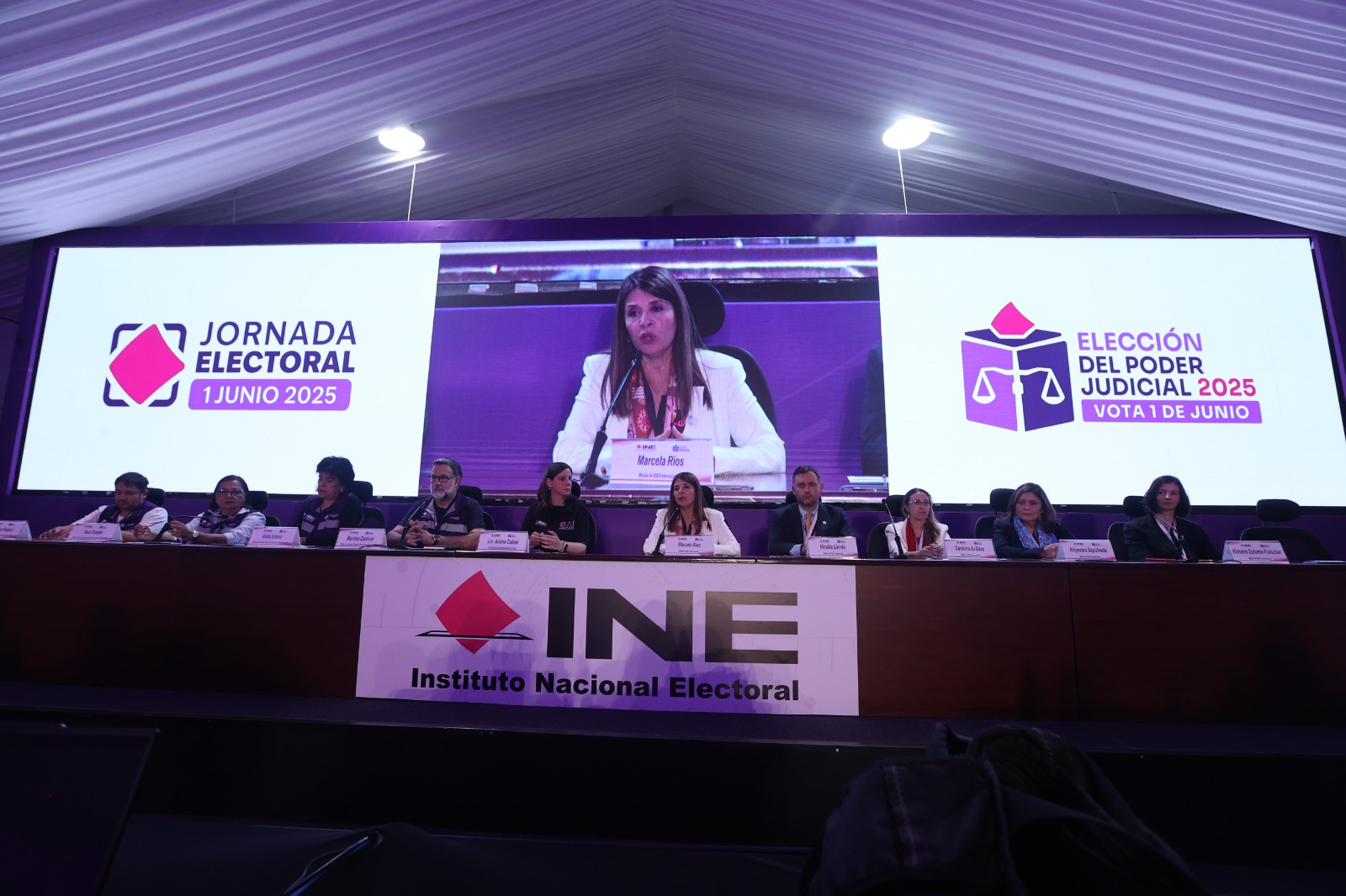 Participantes de la conferencia sentados en el estrado de la Macrosala de prensa