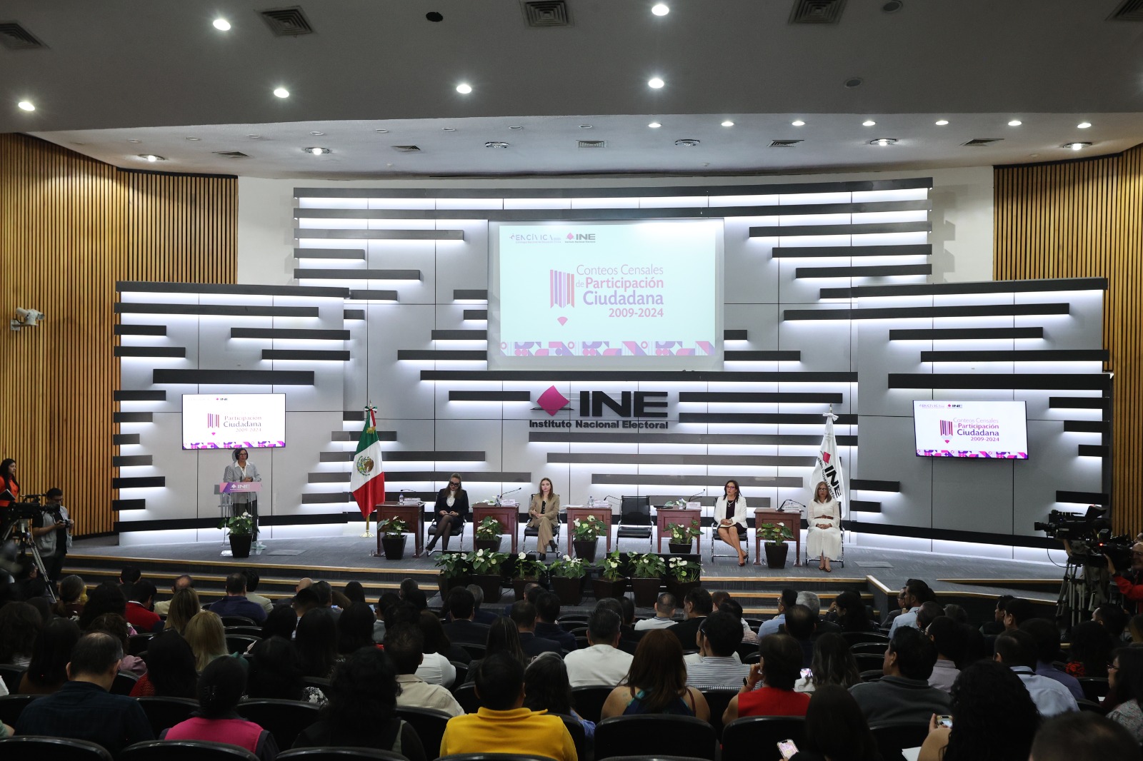 Personas participantes y público asistente al evento, sentados en el auditorio del instituto.