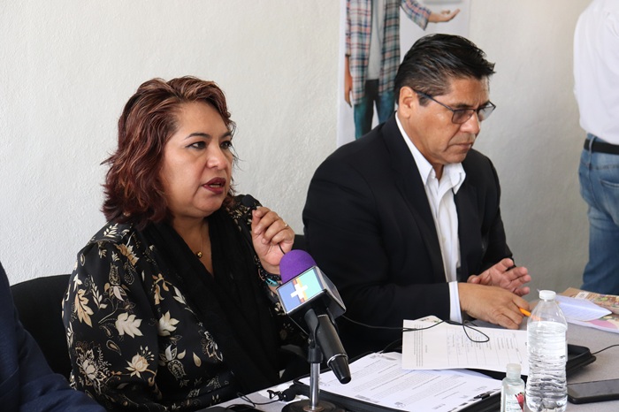 dos personas sentadas frente a un micrófono color morado