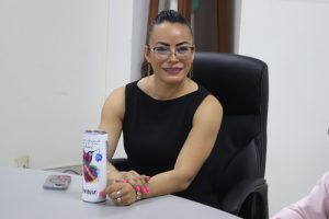 mujer cabello recogido con lentes, vestido negro, sentada con manos entrelazadas