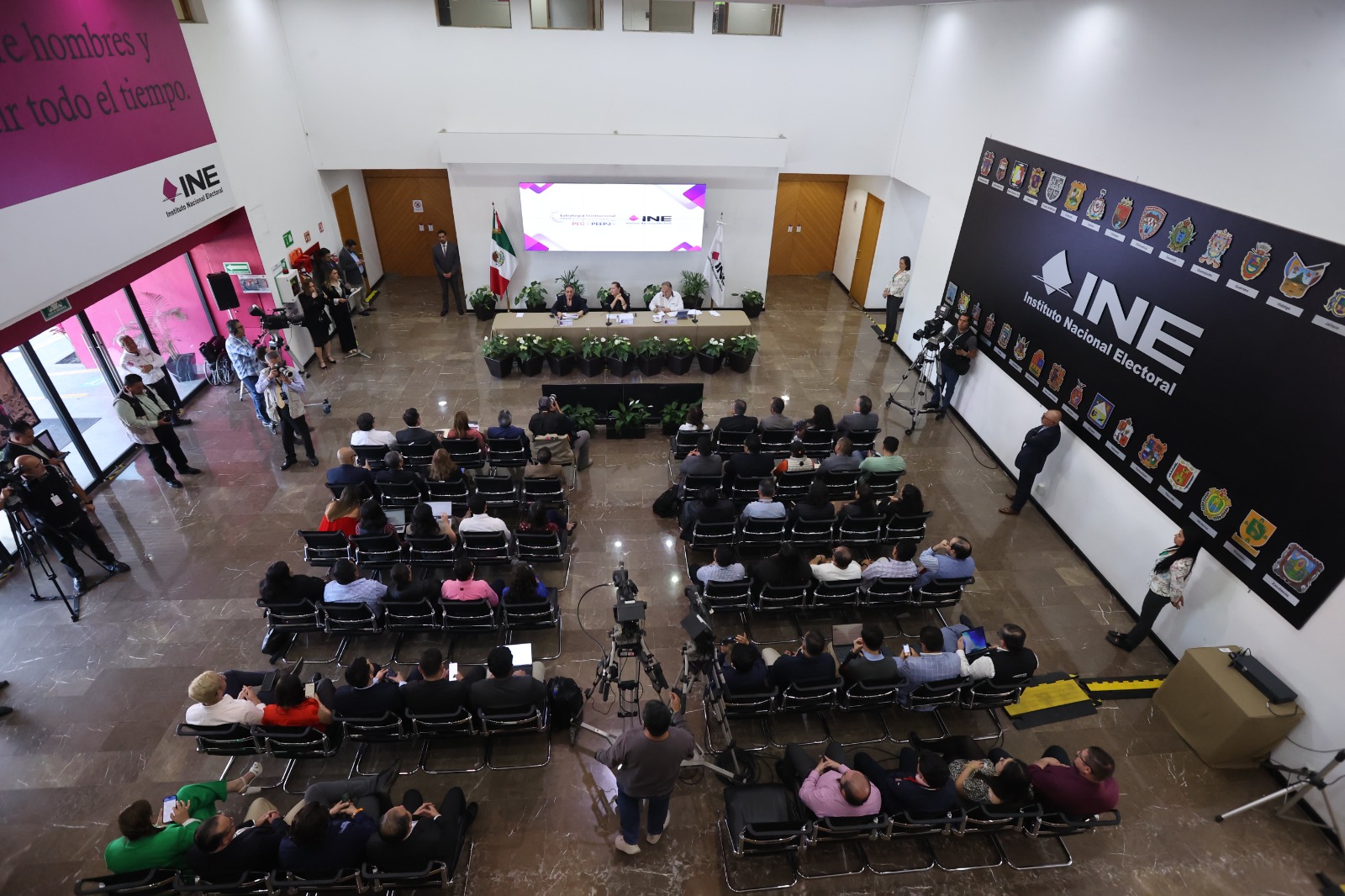 Imagen abierta en el lobby del instituto con las personas participantes paradas al frente de la audiencia.