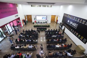 Imagen abierta en el lobby del instituto con las personas participantes paradas al frente de la audiencia.