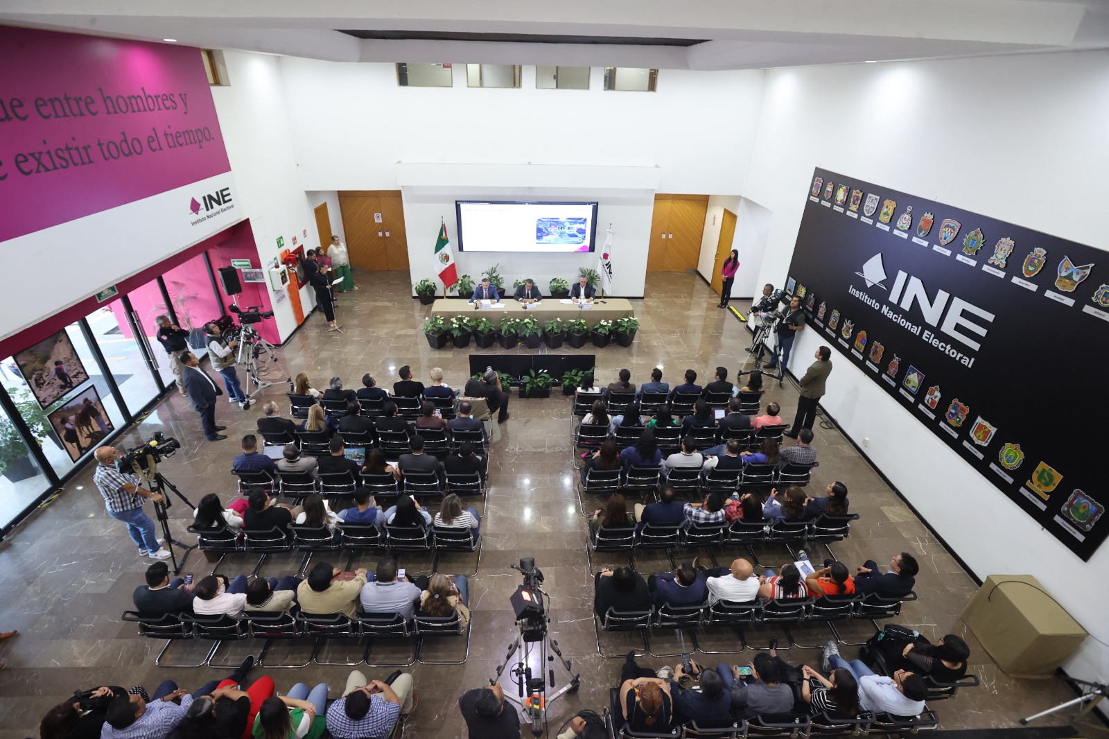 Imagen abierta en el lobby del instituto con las personas participantes paradas al frente de la audiencia.
