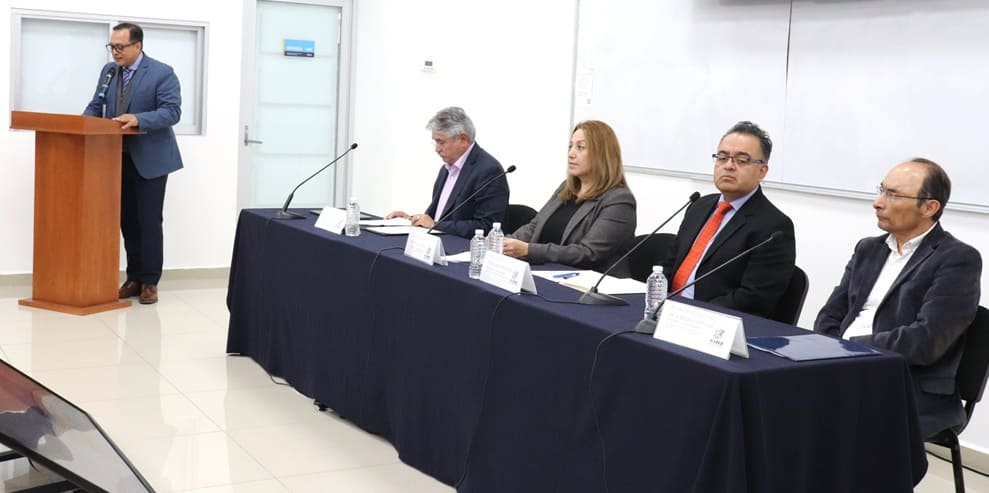 cuatro personas sentadas y uno de pie hablando frente a un micrófono
