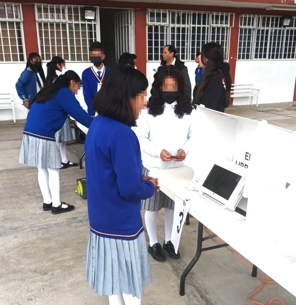 adolescentes mujeres con uniforme azul usando una maquina para votar
