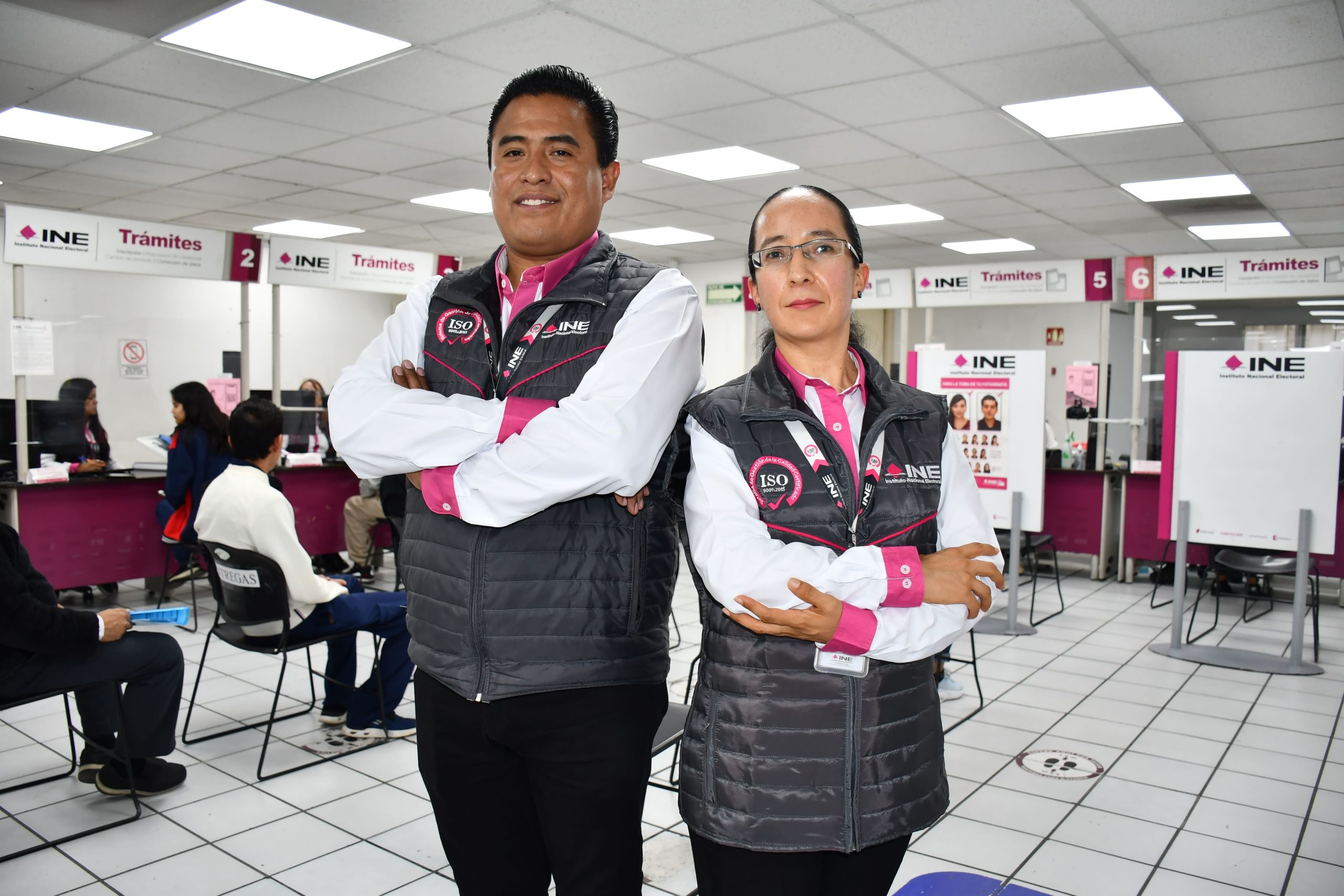 dos personas de pie con brazos cruzados y chaleco negro