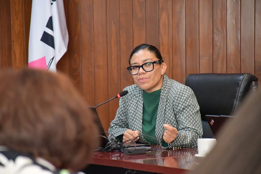 un mujer sentada, cabello recogido hablando frente a un micrófono