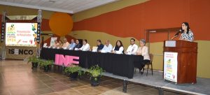 Personas sentadas escuchando a una mujer de pie en un pódium