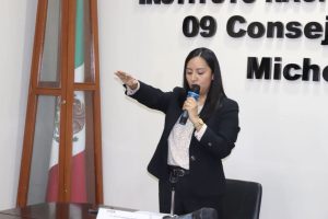 mujer de pie con el brazo derecho extendido hacia enfrente y un micrófono