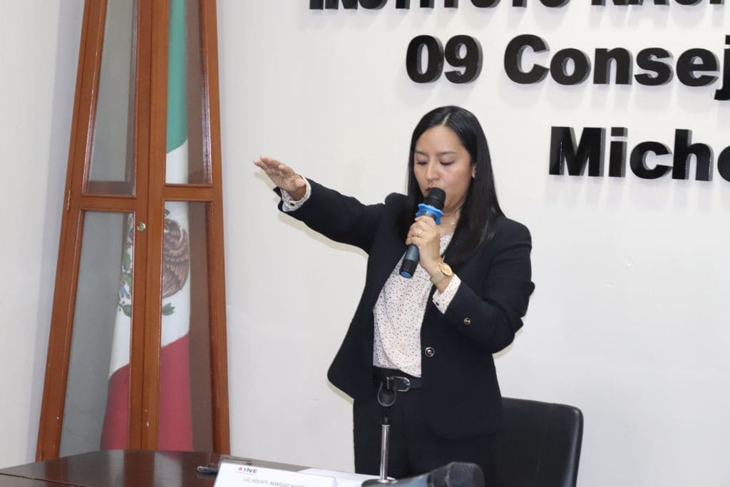 mujer de pie con el brazo derecho extendido hacia enfrente y un micrófono