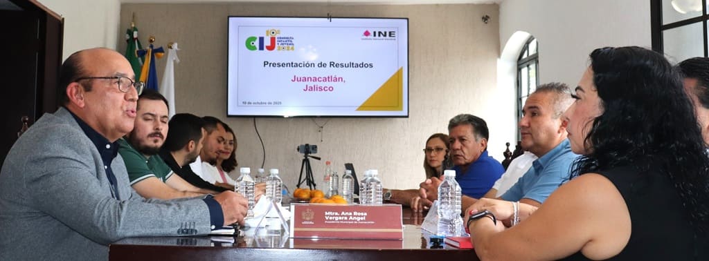 personas sentadas alrededor de una mesa, y al fondo una pantalla