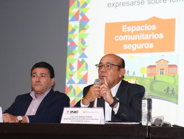 dos hombres sentados, uno de ellos habla por micrófono