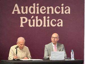 dos hombres sentados, uno frente a un micrófono